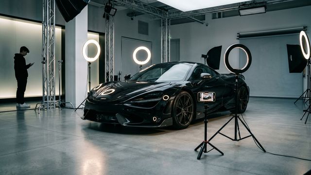 A teenager watches a gleaming sports car being filmed beneath ring lights.